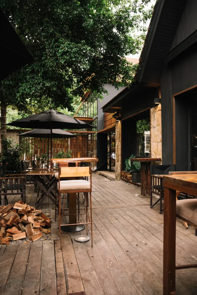 A wooden deck with a table, chairs, and umbrellas, surrounded by trees and greenery. - Deck and patio construction in NJ