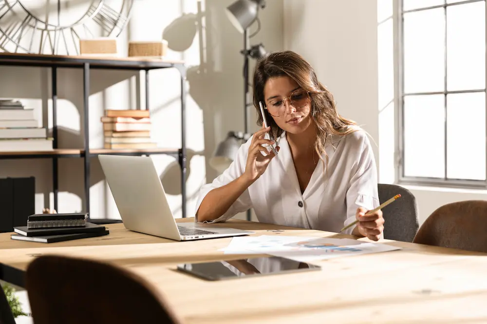 Woman talking on the phone at a desk, planning cost-effective masonry design projects.