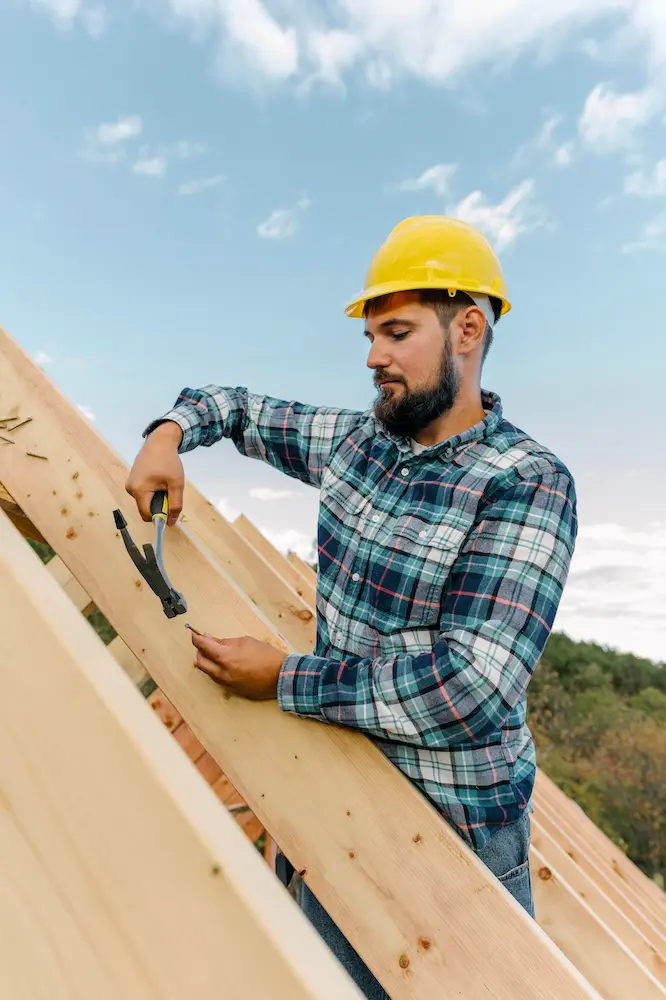 Worker repairing roof with hammer, focusing on common roof repairs.
