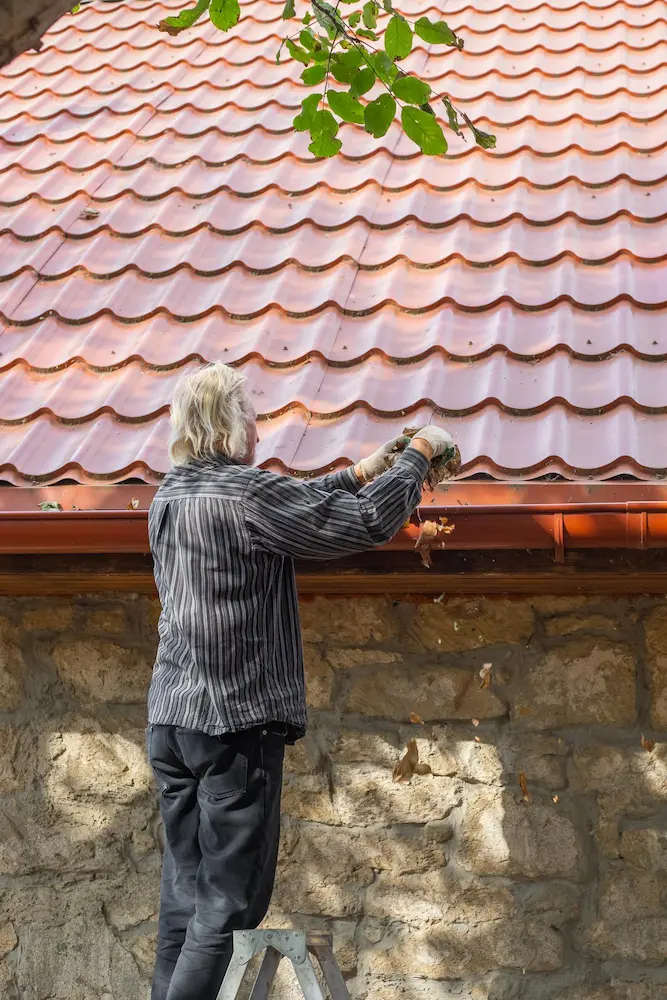 Worker cleaning gutters as part of roof maintenance -Complete Guide to Common Roof Repairs