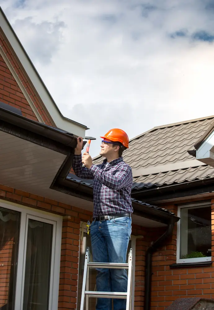 Worker inspecting roof gutter for potential repairs - Complete Guide to Common Roof Repairs